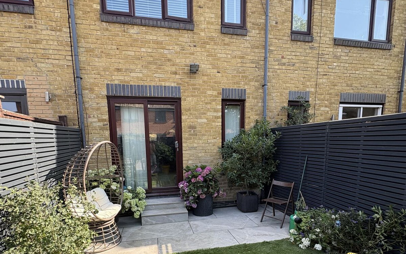 Finished London garden with black slatted fencing and patio, ready for autumn