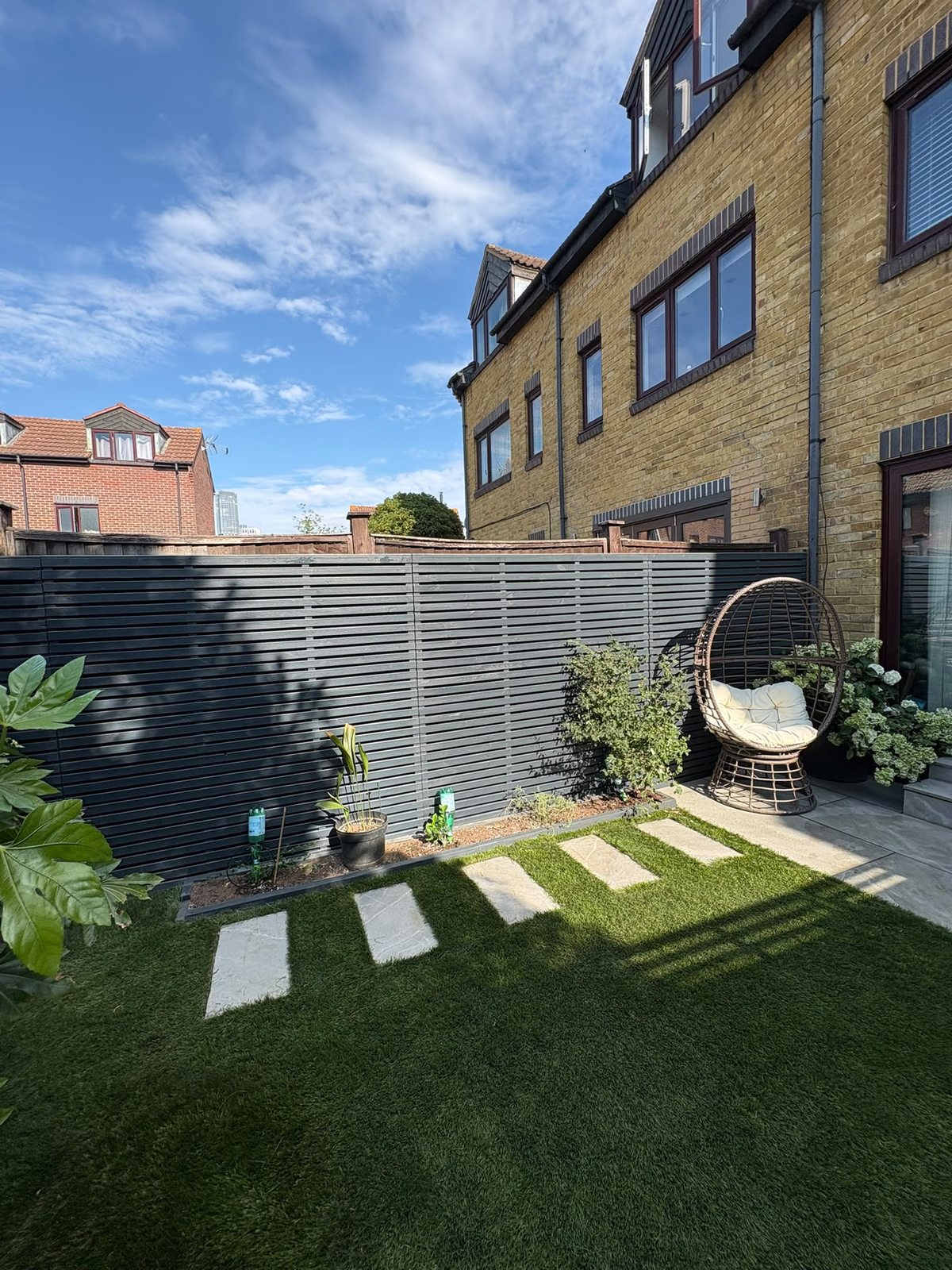 Rear garden with black slatted fencing, stone patio and artificial lawn, Rotherhithe SE16